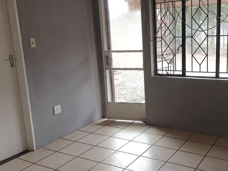 An empty living area featuring tiled flooring, a security gate, and burglar bars on the windows, providing a blank canvas for interior updates.