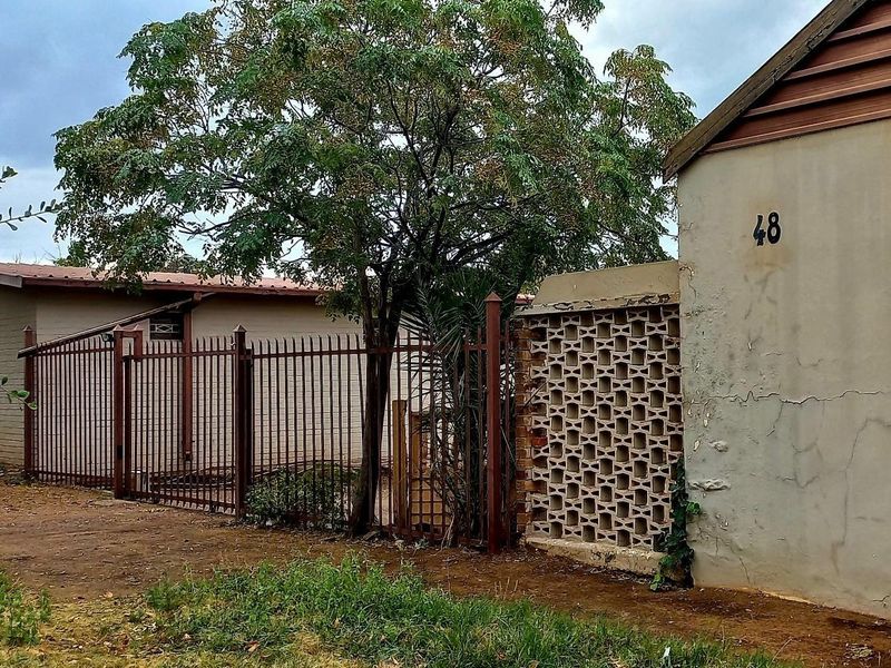 Front exterior view of the property featuring a metal security fence, decorative breeze block wall, and a plastered facade with visible wear.