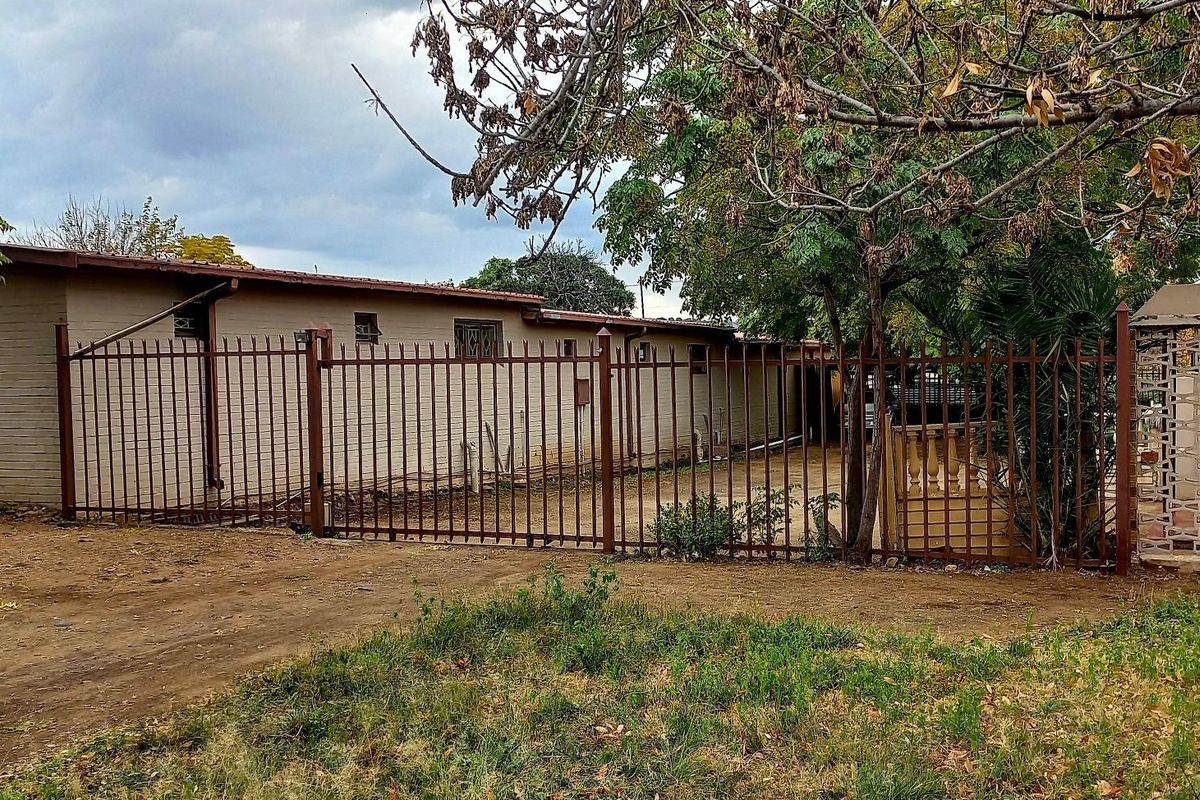 Rear exterior view of the property featuring a brick facade, tiled roof, and metal perimeter fencing with an unpaved yard area.