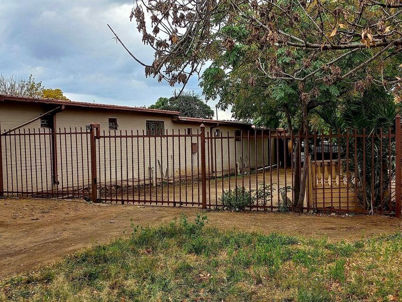 Rear exterior view of the property featuring a brick facade, tiled roof, and metal perimeter fencing with an unpaved yard area.