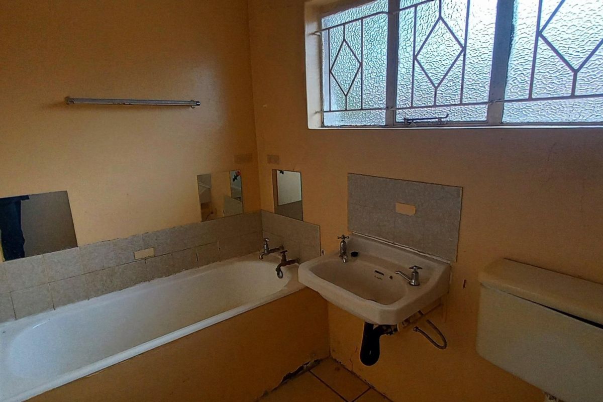 A dated bathroom featuring a bathtub, wall-mounted basin, and toilet, requiring renovation to update finishes and address visible wear.