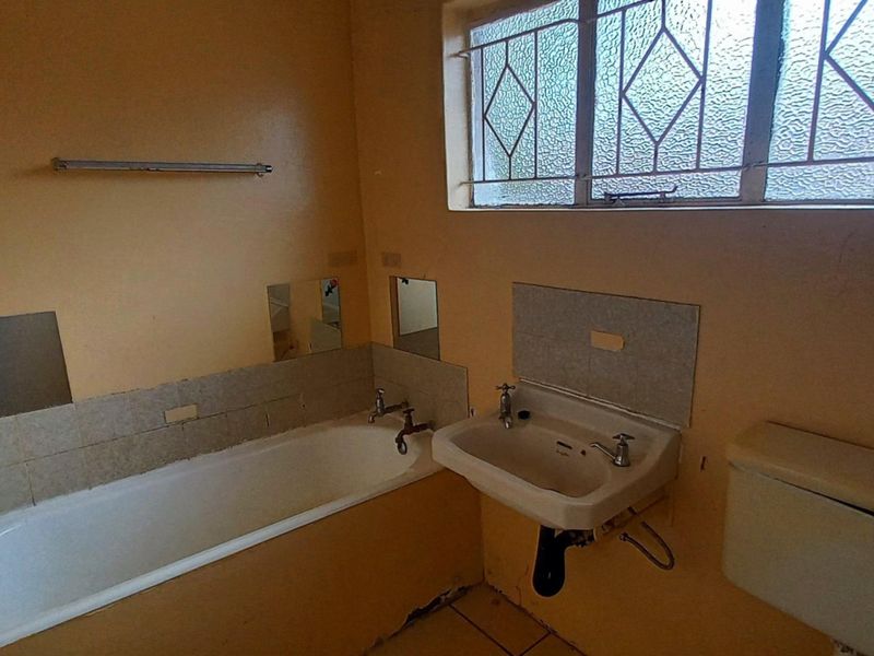 A dated bathroom featuring a bathtub, wall-mounted basin, and toilet, requiring renovation to update finishes and address visible wear.