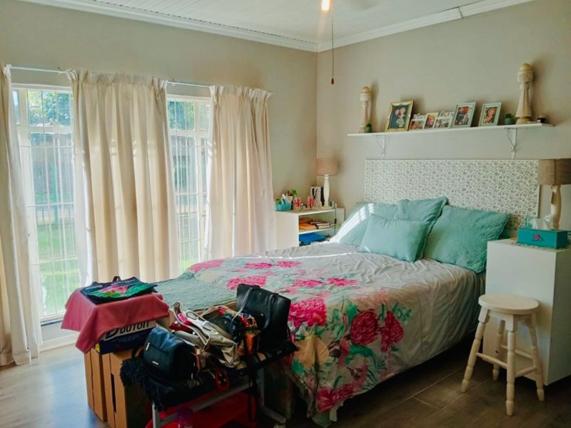 A bedroom featuring laminate flooring, a ceiling fan, and a sliding glass door with security gate providing access to the exterior.