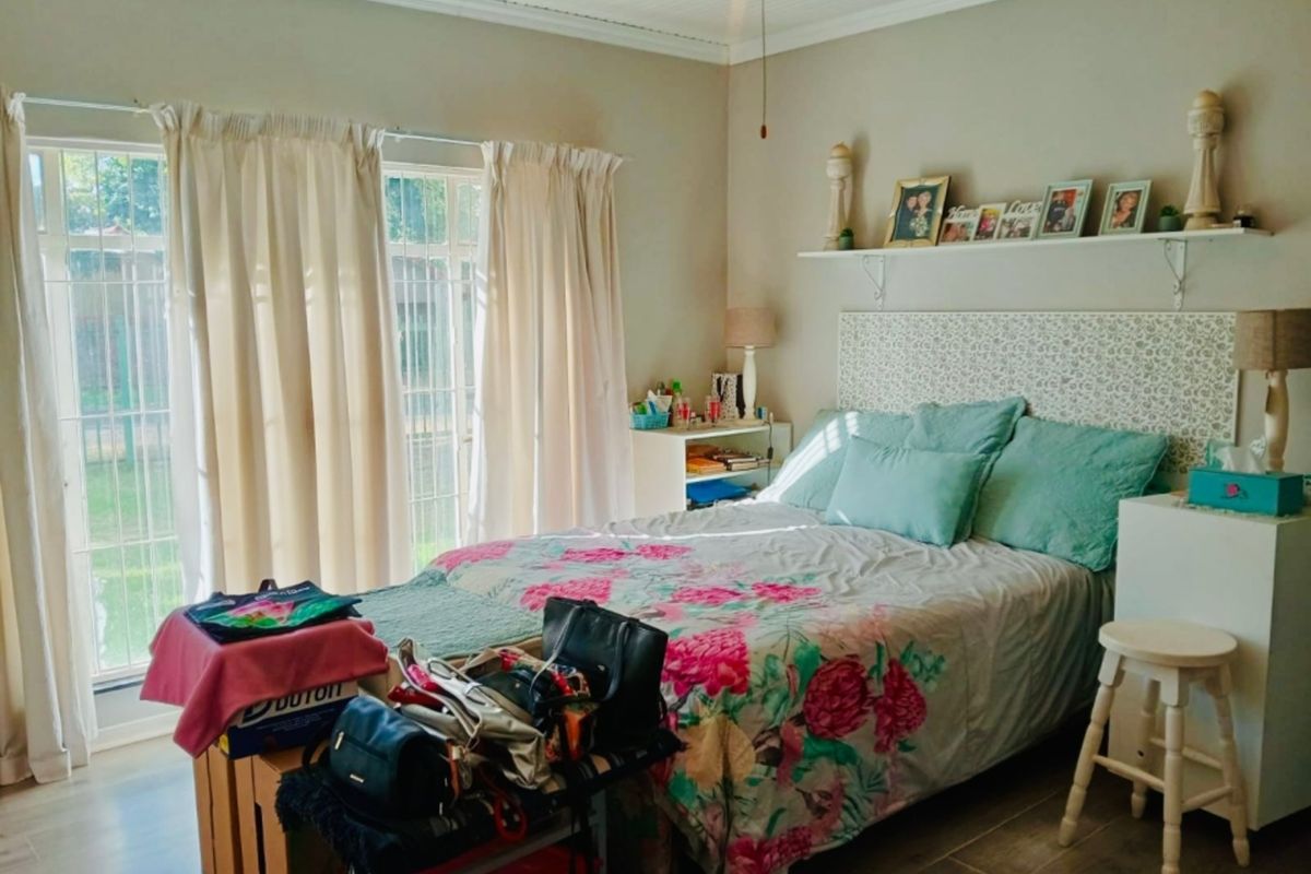 A bedroom featuring laminate flooring, a ceiling fan, and a sliding glass door with security gate providing access to the exterior.
