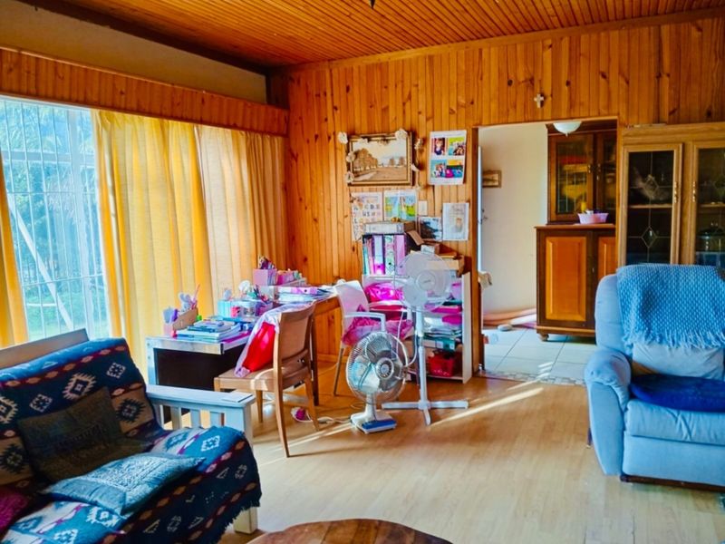 A living room featuring traditional timber wall paneling and ceiling with laminate flooring, offering a warm, rustic aesthetic with potential for modern updates.