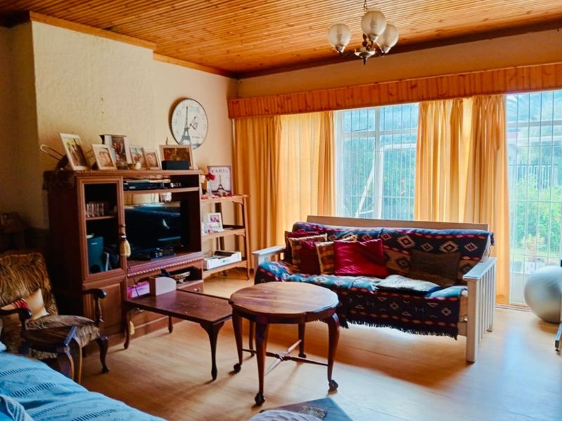 A living room featuring a timber-clad ceiling, laminate flooring, and large windows that provide natural light.