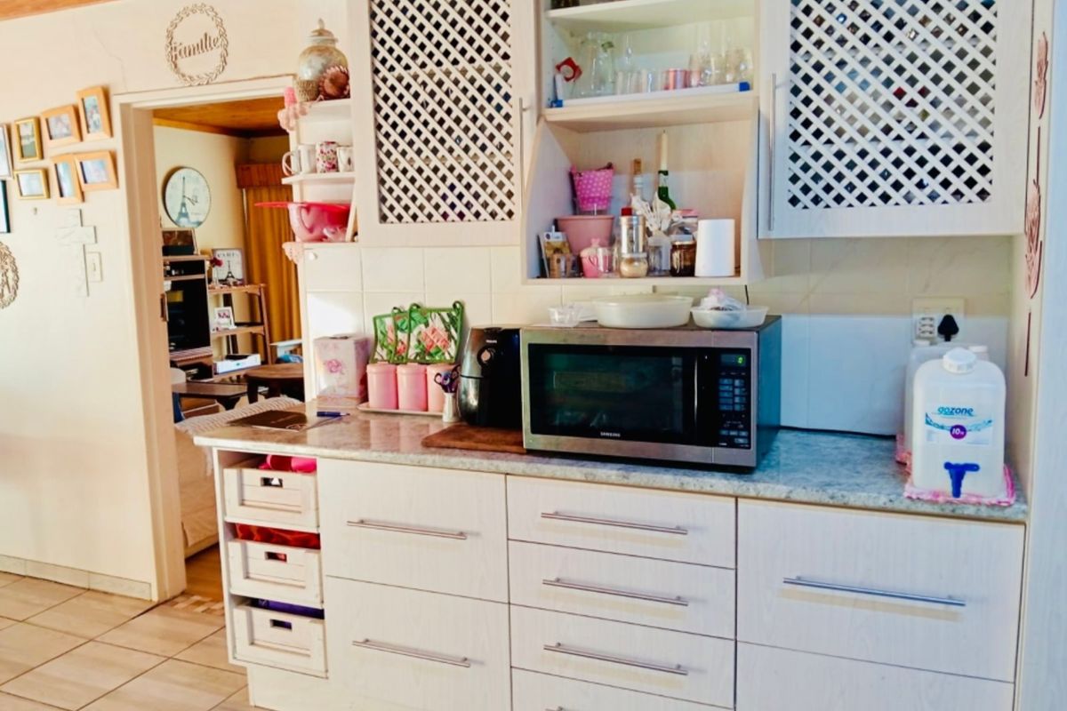 A functional kitchen area featuring white cabinetry, laminate countertops, and tiled flooring, with an adjacent view into the living space.