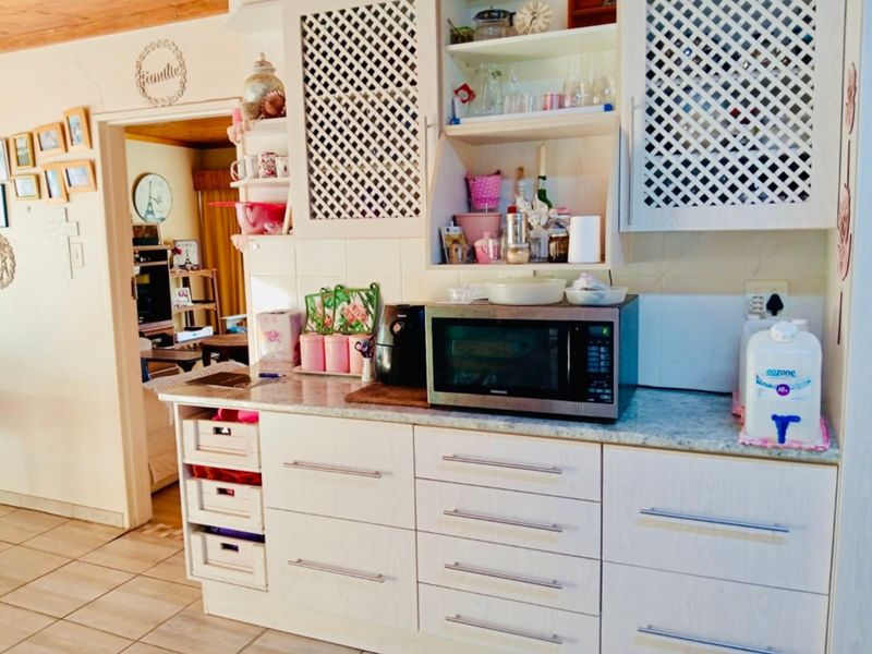 A functional kitchen area featuring white cabinetry, laminate countertops, and tiled flooring, with an adjacent view into the living space.
