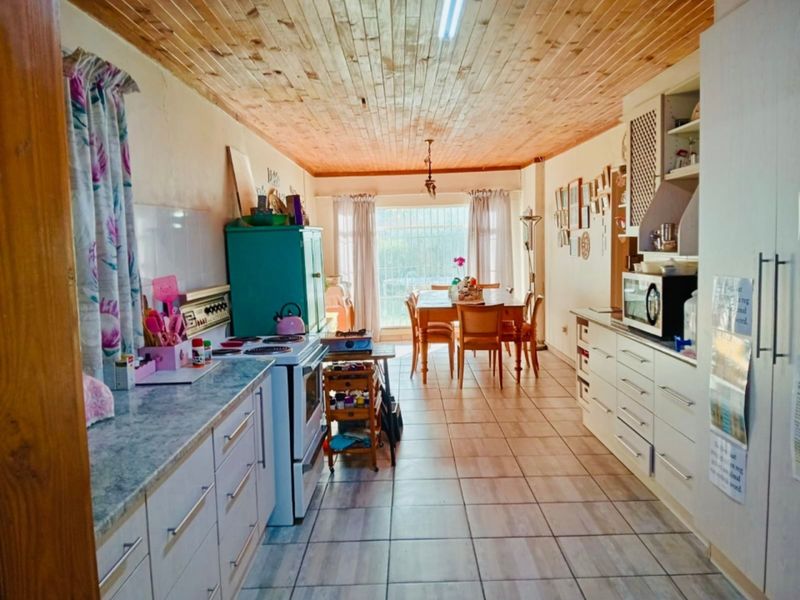 Open-plan kitchen and dining area featuring tiled floors, timber ceiling, and functional built-in cabinetry with laminate countertops.