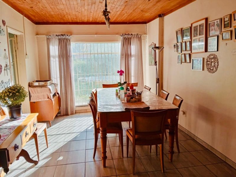 A dining room featuring a warm timber ceiling, tiled flooring, and a large window with security bars allowing natural light into the space.