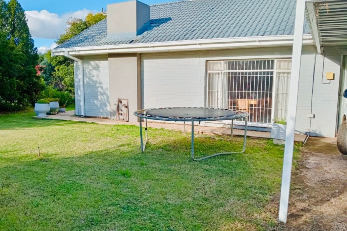 Rear view of the house featuring a tiled roof, chimney, and sliding glass doors with security bars, overlooking a private garden area.