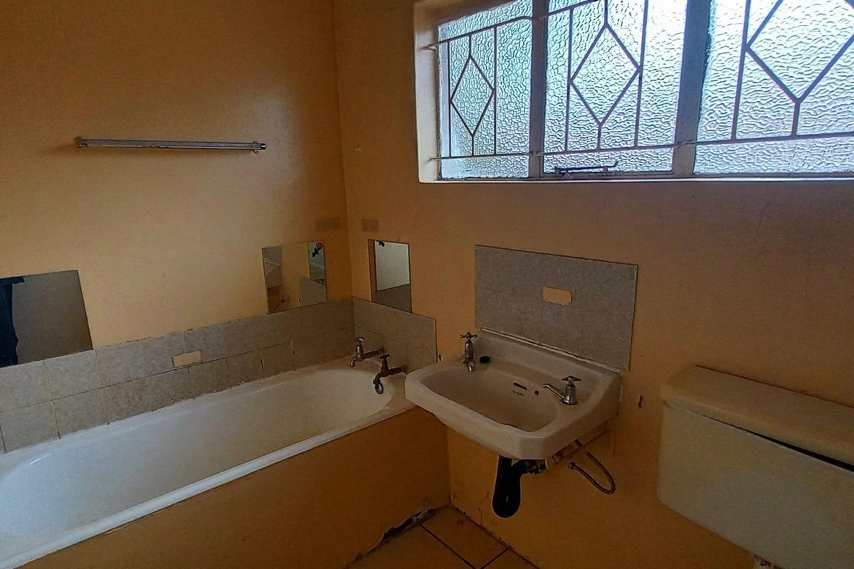 A dated bathroom featuring a bathtub, wall-mounted basin, and toilet cistern, requiring renovation and cosmetic updates to improve its condition.