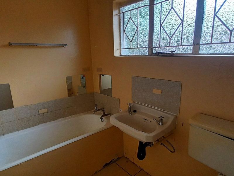 A dated bathroom featuring a bathtub, wall-mounted basin, and toilet cistern, requiring renovation and cosmetic updates to improve its condition.