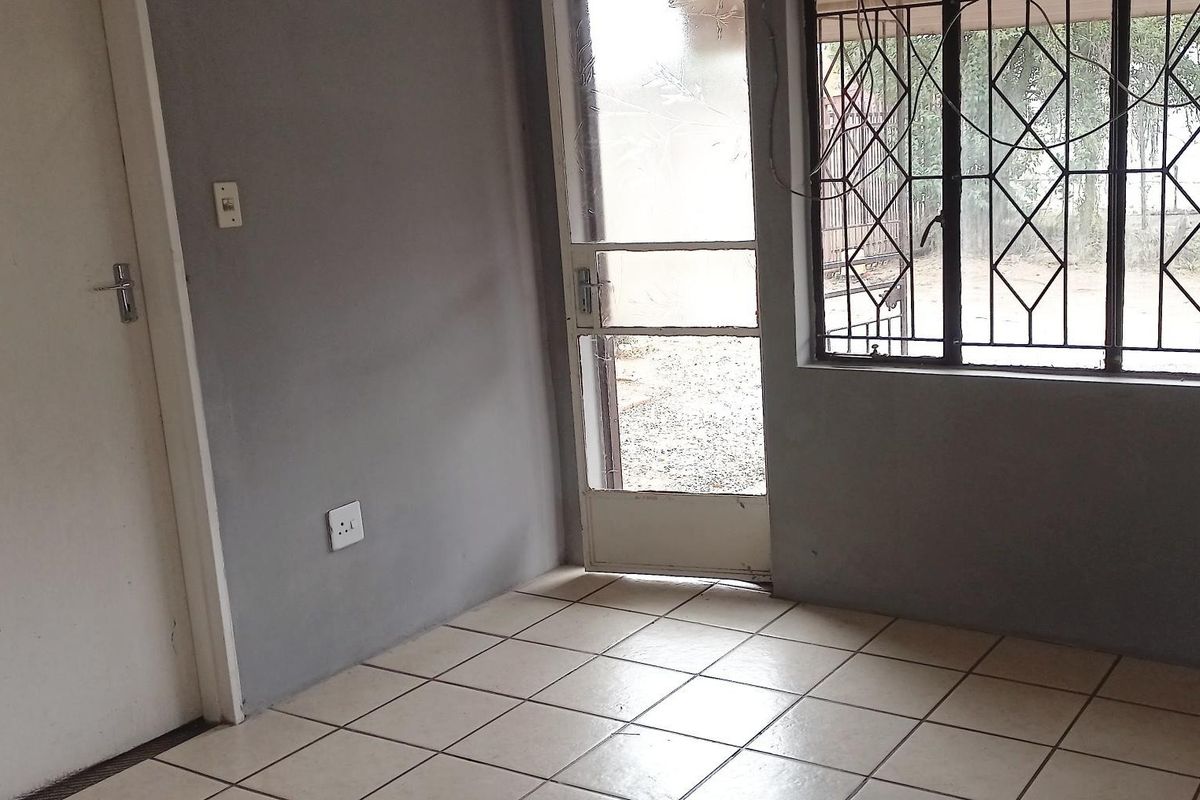 An empty living area featuring tiled flooring, a security gate, and burglar bars on the windows, offering a blank canvas for renovation.