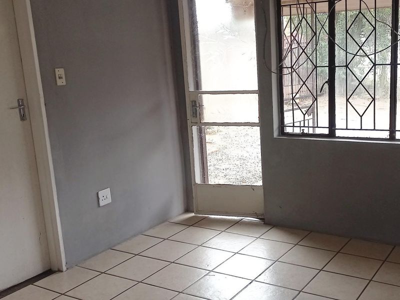 An empty living area featuring tiled flooring, a security gate, and burglar bars on the windows, offering a blank canvas for renovation.