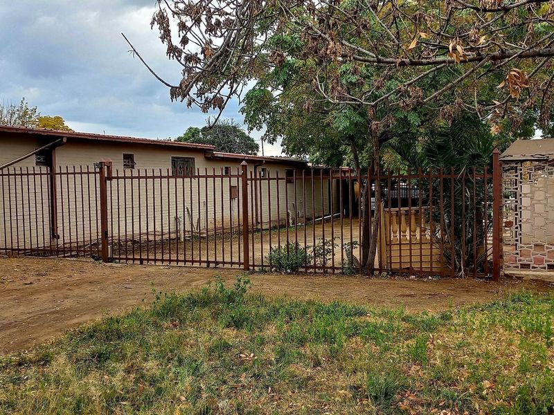 Front exterior view of the cluster property featuring a metal security fence, brick facade, and established trees on the property grounds.