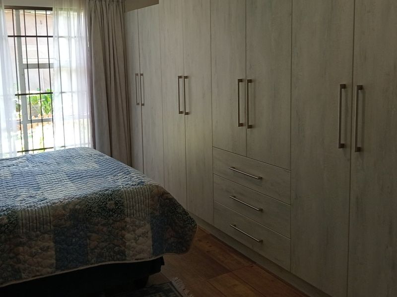 A well-maintained bedroom featuring extensive floor-to-ceiling built-in cupboards, timber flooring, and natural light through a window with security bars.