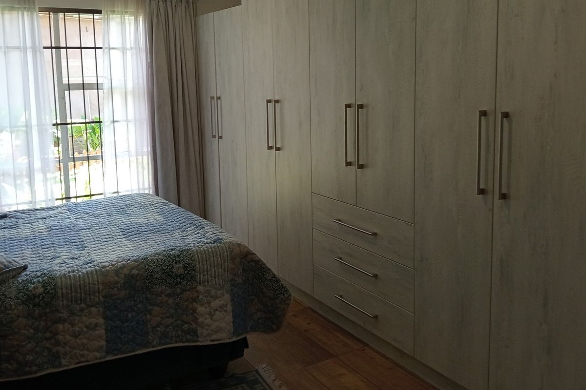 A well-maintained bedroom featuring extensive floor-to-ceiling built-in cupboards, timber flooring, and natural light through a window with security bars.