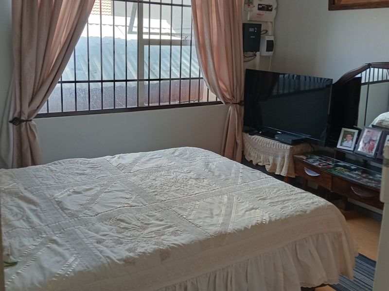 A functional bedroom featuring laminate flooring and security burglar bars on the window, providing a comfortable and secure living space.