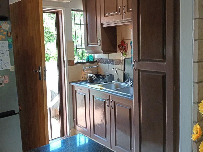 A compact kitchen area featuring dark wood-finish cabinetry, a double sink, and a tiled backsplash with direct access to an outdoor area.