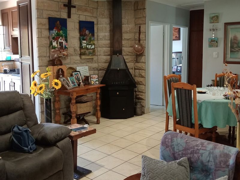 Open plan living and dining area featuring a prominent stone fireplace and tiled flooring, with an adjacent kitchen visible in the background.