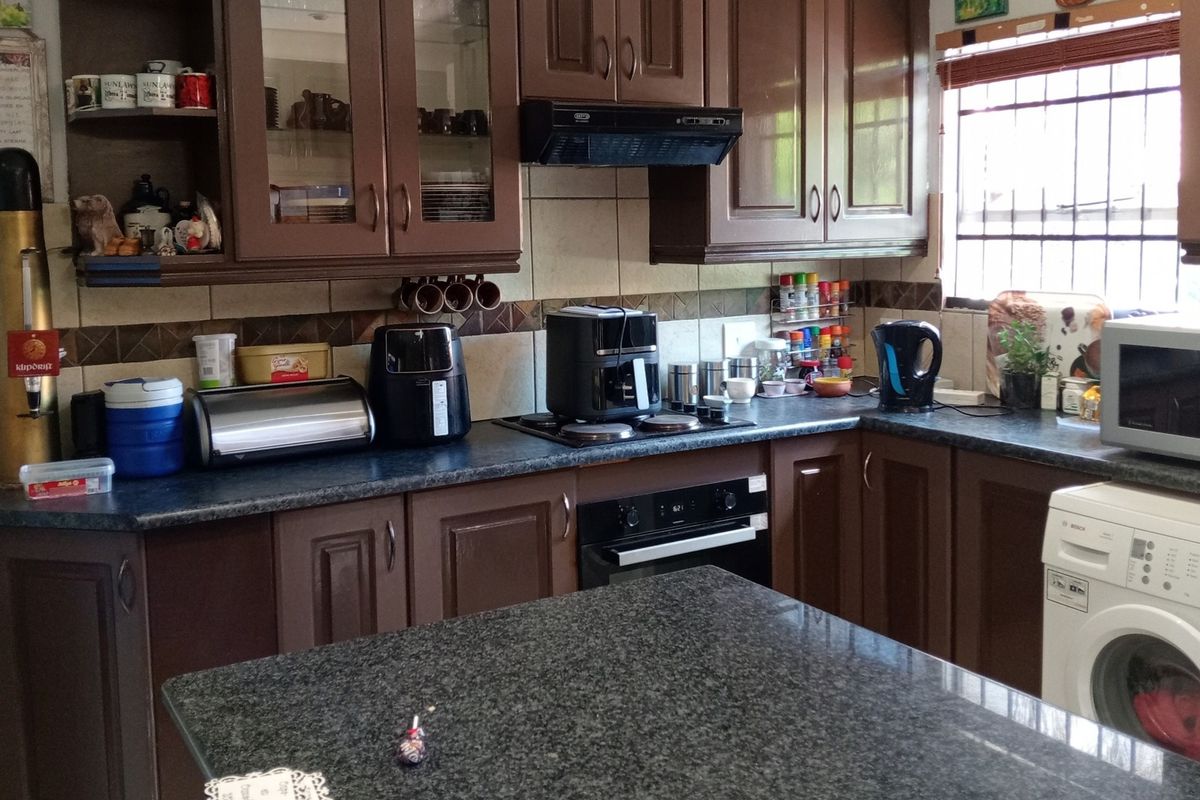 A functional kitchen featuring dark wood cabinetry, granite countertops, built-in oven, electric hob, and a tiled backsplash with integrated security bars on the window.