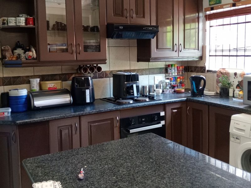 A functional kitchen featuring dark wood cabinetry, granite countertops, built-in oven, electric hob, and a tiled backsplash with integrated security bars on the window.