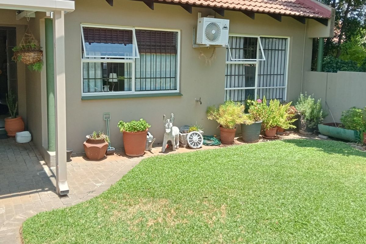 A rear exterior view of the townhouse featuring a paved patio area, a small lawn, and a wall-mounted air conditioning unit.