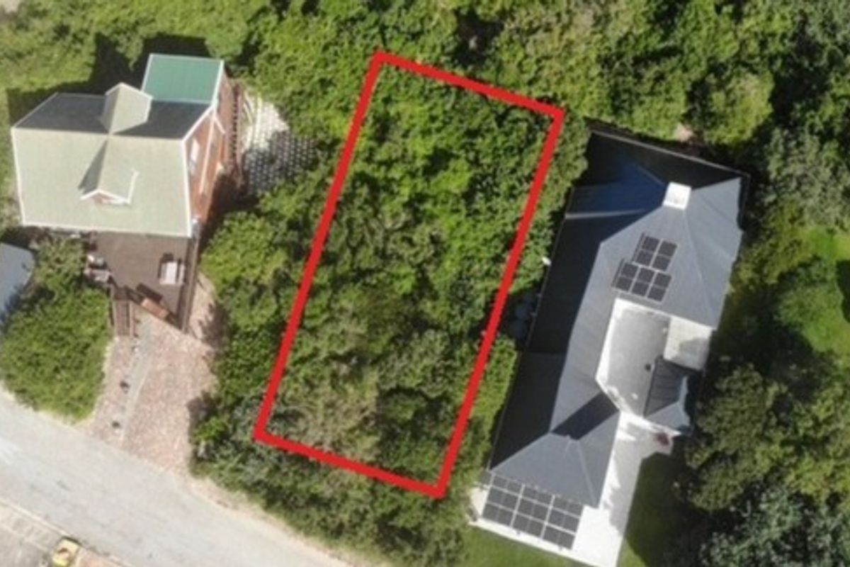 An aerial view of a vacant residential plot highlighted in red, situated between two existing properties with established vegetation.