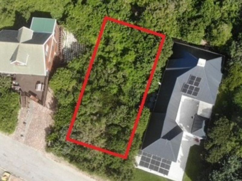 An aerial view of a vacant residential plot highlighted in red, situated between two existing properties with established vegetation.