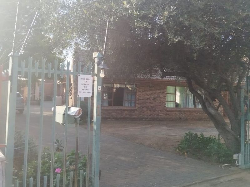 Front view of the guest house property featuring a brick facade, paved driveway, and secure metal gate with electric fencing.