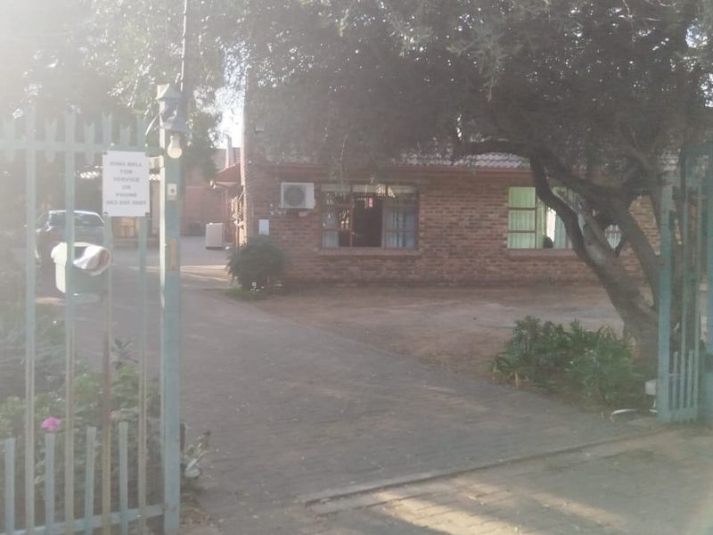 Front view of the guest house property featuring a brick facade, paved driveway, and secure metal gate entrance.