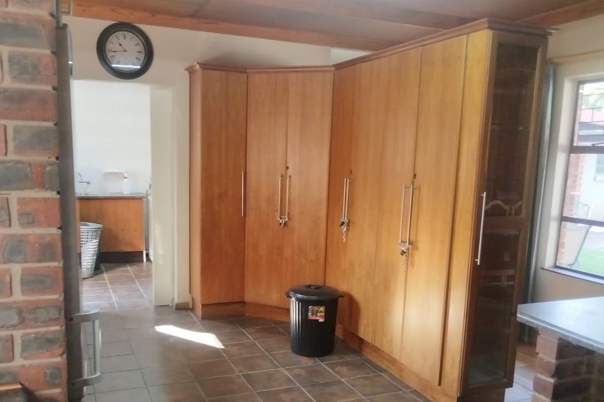 A kitchen area featuring extensive built-in wooden cabinetry, exposed brick accents, and tiled flooring, with an adjacent scullery visible through the doorway.