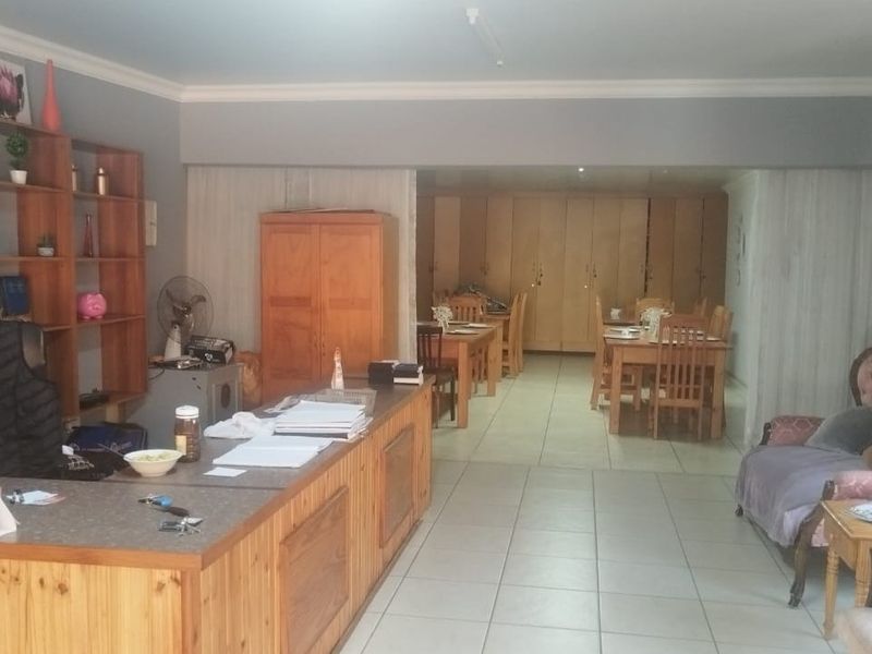 Open-plan guest house reception and dining area featuring built-in wooden cabinetry, a reception counter, and tiled flooring throughout.