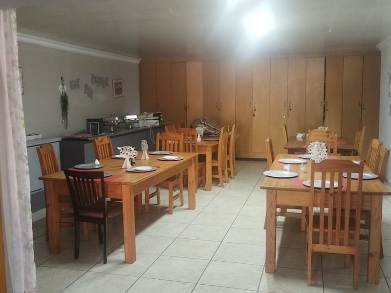 A spacious dining area featuring tiled flooring, extensive built-in cabinetry, and cove cornice detailing, suitable for guest house dining or communal use.