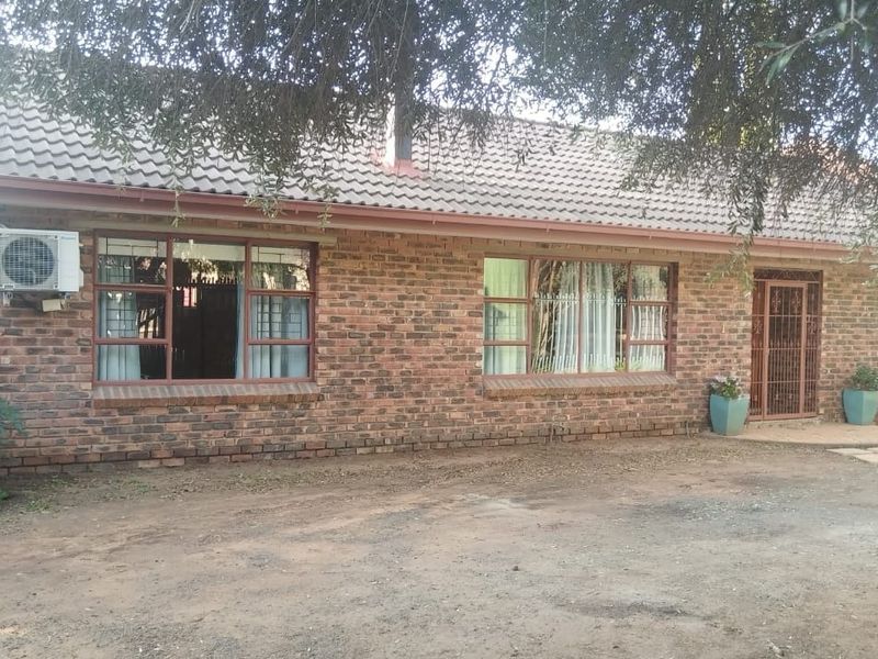 Front elevation of a face brick guest house featuring a tiled roof, security gate, and exterior air conditioning unit.
