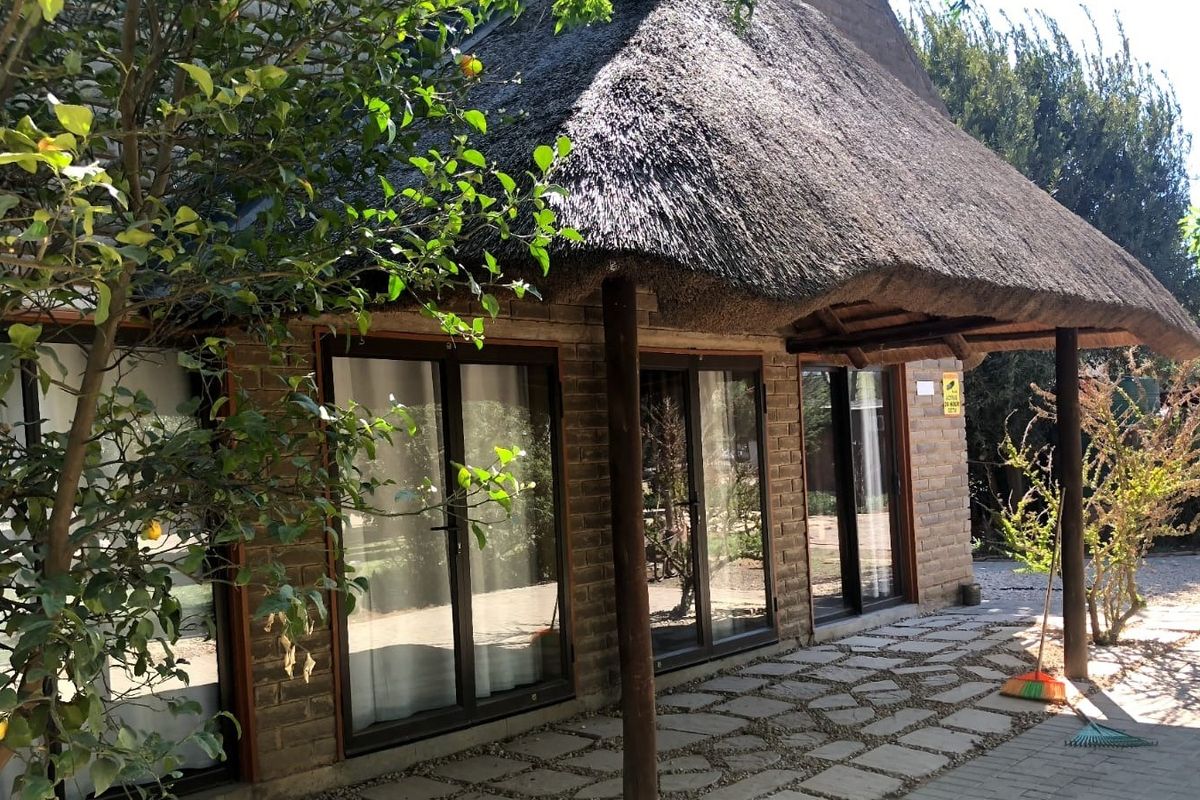Rear exterior view of a lodge featuring a traditional thatch roof, exposed brick walls, and sliding glass doors opening onto a paved patio area.