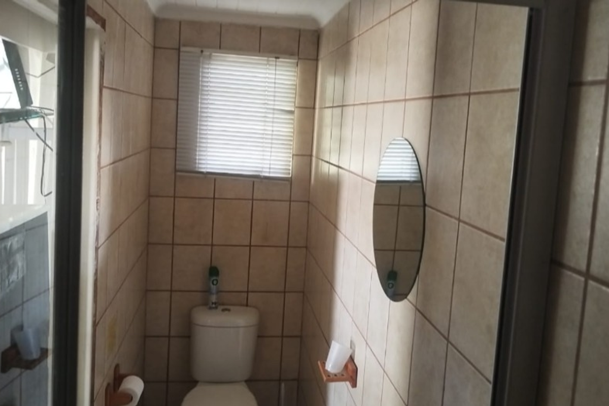 A compact bathroom featuring tiled walls, a standard toilet, and a window with fitted blinds.