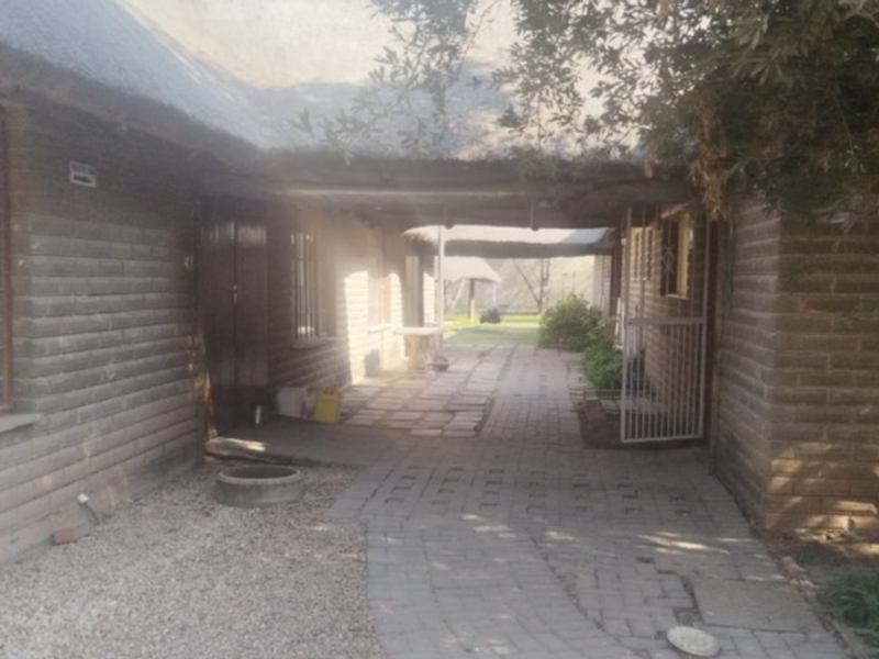 A view of the lodge exterior featuring a covered walkway, thatched roofing, and paved pathways leading to the rear garden area.
