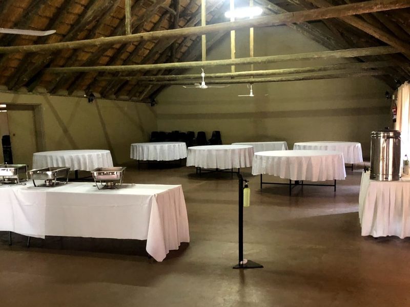 Spacious lodge hall featuring exposed timber roof trusses, a traditional thatched ceiling, and durable concrete flooring, suitable for events or communal gatherings.