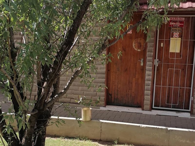 Exterior view of a lodge building featuring a brick facade, timber door, and a security gate with signage.