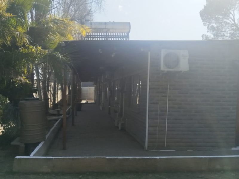Rear exterior view of the lodge featuring a covered patio, brick facade, solar water heating system, and wall-mounted air conditioning unit.