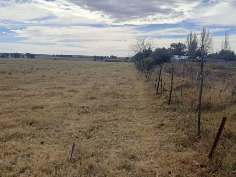 Expansive open farmland view featuring a traditional barbed wire boundary fence with wooden posts stretching across the property.