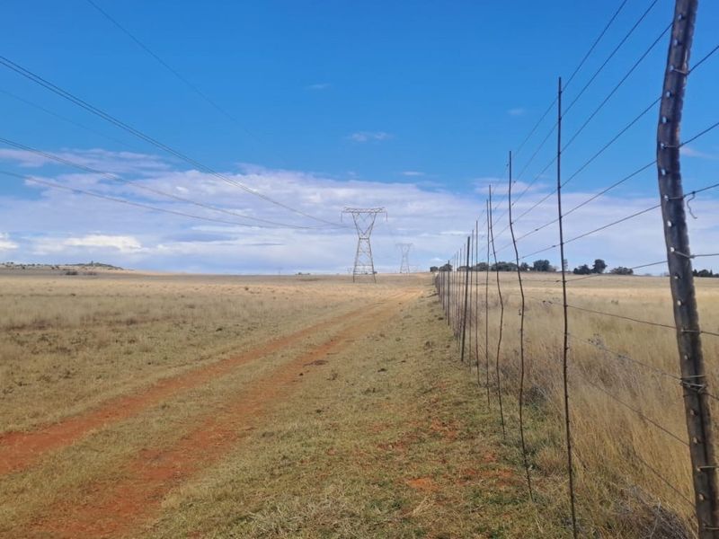 Expansive open farm land featuring a dirt access track and perimeter wire fencing with visible overhead power lines.