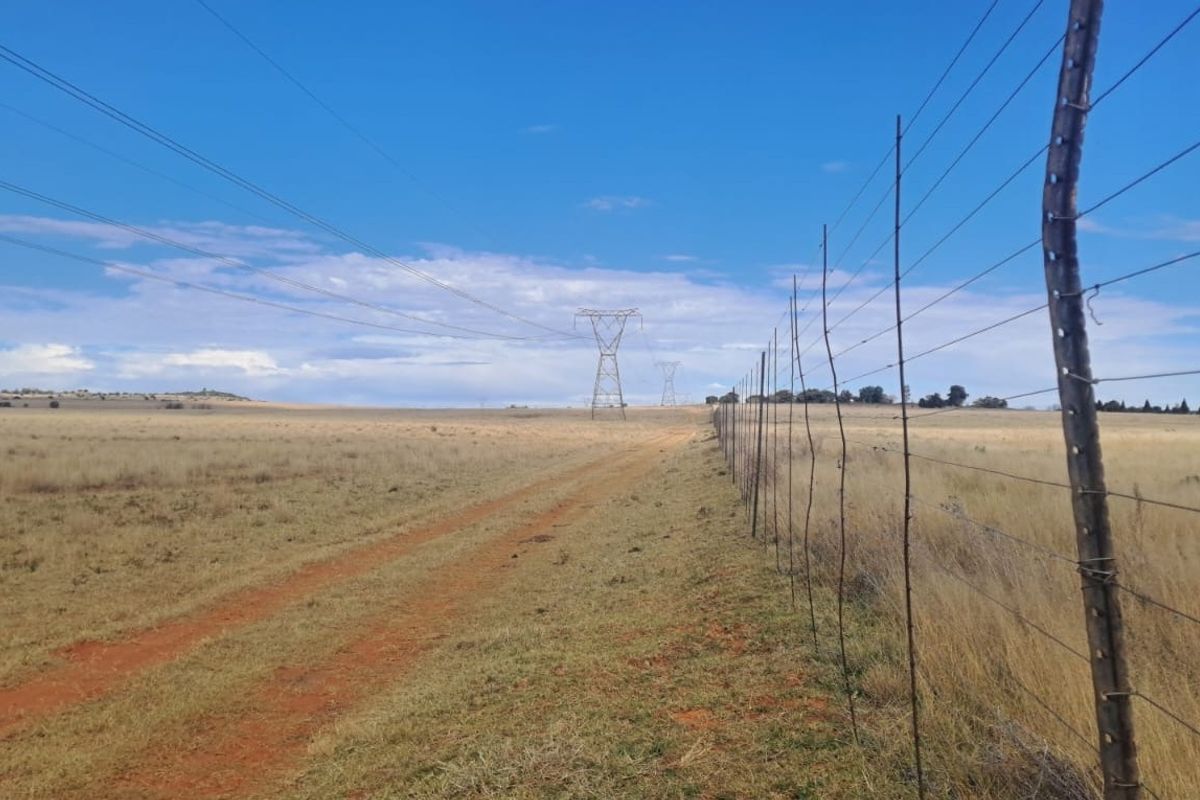 Expansive open farm land featuring a dirt access track and perimeter wire fencing with visible overhead power lines.