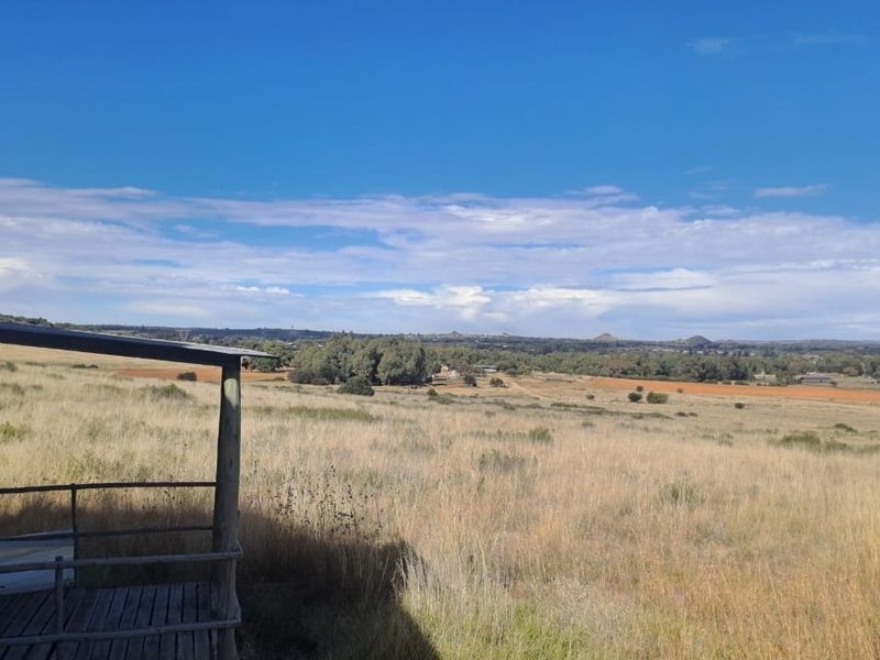 Expansive rural landscape view overlooking open fields and natural vegetation, captured from a rustic timber deck structure.