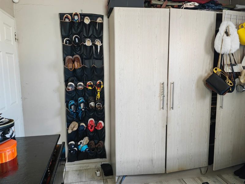 A bedroom interior featuring a light-toned built-in wardrobe with metal handles and visible wall wear.