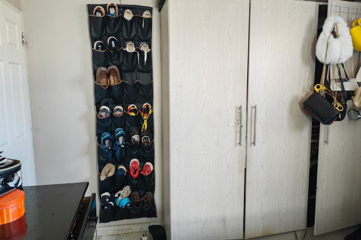 A bedroom interior featuring a light-toned built-in wardrobe with metal handles and visible wall wear.