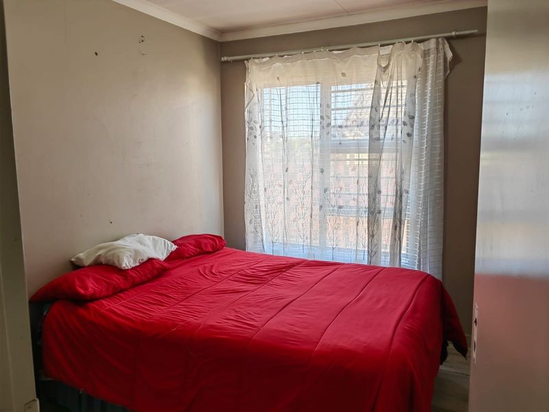 A bedroom featuring tiled flooring, a window with security bars, and a curtain rod. The walls show signs of wear and require maintenance.