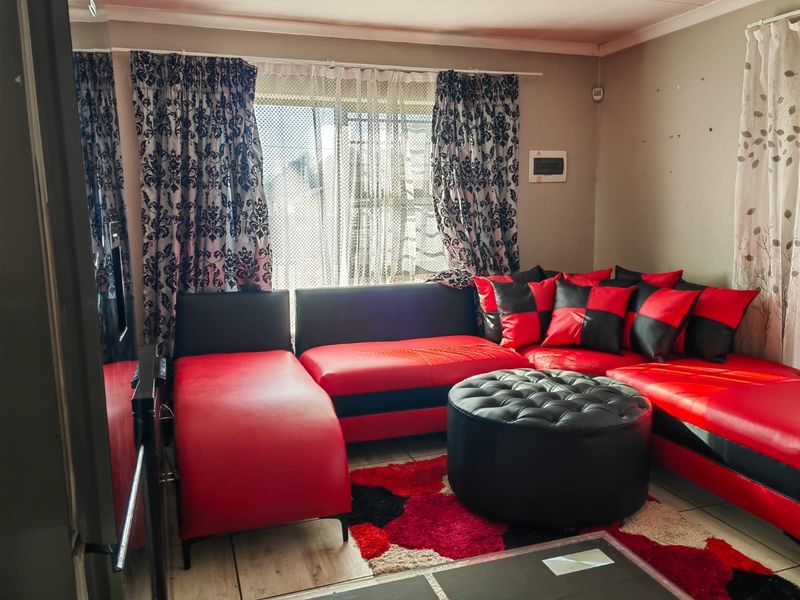 A living room area featuring tiled flooring and a wall-mounted security alarm keypad, requiring minor cosmetic wall repairs.